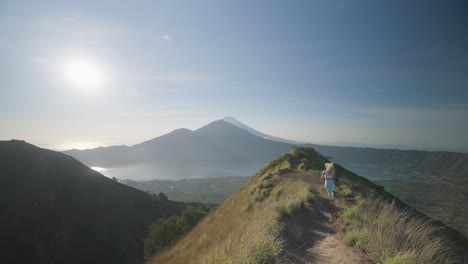 Sportive-blond-woman-running-on-mountain-trail-ridge-towards-lookout,-sense-of-freedom,-Bali