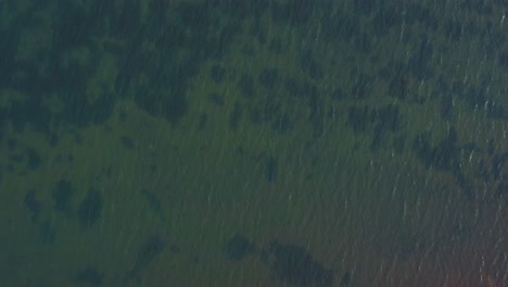 Smooth-drone-flight-over-flowing-water-with-little-waves-of-a-lake,-looking-down-to-the-clear-ground