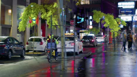 Taxi-Y-Repartidor-De-Comida-En-Bicicleta-Viajando-En-La-Calle-Por-La-Noche-En-Sydney,-Nsw,-Australia