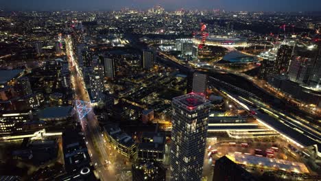Futuristische-Stratford-Luxuswolkenkratzer-In-Der-Innenstadt,-Leuchtende-Straßen-Bei-Nacht,-Luftaufnahme,-Langsamer-Vorwärtsflug