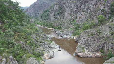 Low-aerial-flight-down-rugged-river-canyon-to-riverside-camp-site