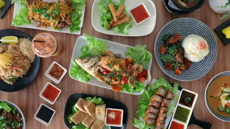 Male-hand-placing-thai-cuisine-fried-fish-onto-flat-lay-food-arrangement