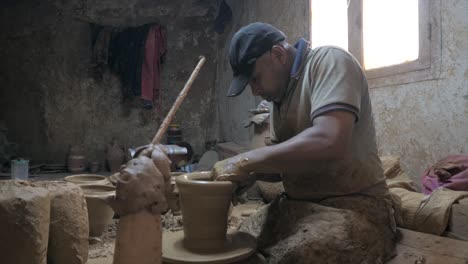 Side-view-of-potter-making-and-shaping-clay-vessel-rotating-on-potters-wheel