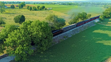 Aerial-View-of-an-Antique-Steam-Engine-and-Passenger-Coaches-Traveling-Along-Countryside-Blowing-Smoke-and-Drone-Traveling-in-Front-of-It-as-it-Crosses-Over-a-Small-Bridge-on-a-Sunny-Summer-Day