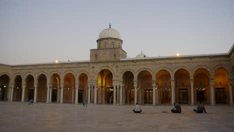 Muslim-People-Sitting-On-The-Ground-In-Front-Of-Al-Zaytuna-Mosque-In-Tunis,-Tunisia-At-Dusk