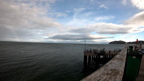 Time-lapse-of-people-fishing-off-Llandudno-wooden-pier-overlooking-rainbow-overcast-ocean