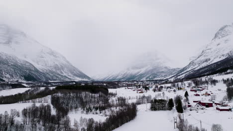 Misty-mountains-and-snowed-in-village-in-white-Manndalen-valley,-winter-aerial
