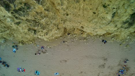 Tourists-on-Bridport-beach-Aerial-view-descending-West-bay-sandstone-cliffs,-Dorset