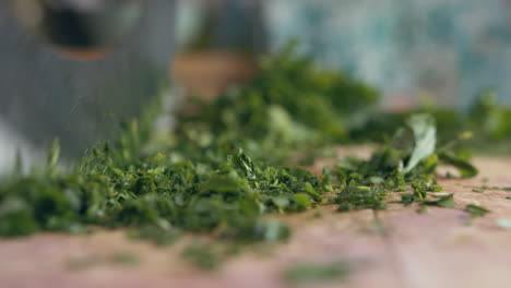 Close-up-side-view-of-woman's-hand-fast-chopping-green-parsley-with-an-Italian-mincing-knife-sharp-knife-on-a-wooden-board-in-her-kitchen