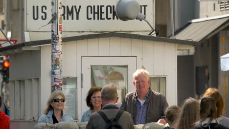 Una-Feliz-Pareja-De-Ancianos-Tomando-Una-Fotografía-Frente-Al-Monumento-Checkpoint-Charlie-En-Berlín,-Alemania