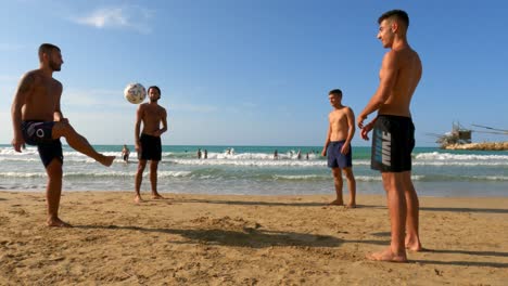 Group-of-friends-have-fun-playing-soccer-on-sandy-beach-at-Punta-Penna-in-Abruzzo,-Italy