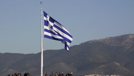 Flag-of-Greece-at-the-top-of-the-Acropolis-and-over-tourists-as-they-sightsee-the-mountains-around-Athens