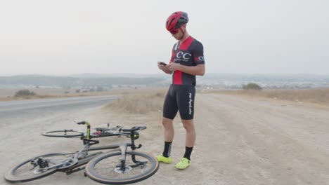 Joven-Atleta-Profesional-Arreglando-El-Neumático-De-Su-Bicicleta-Revisando-Su-Dispositivo