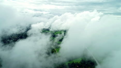 Beim-Überfliegen-Sind-Hinter-Den-Wolken-Leuchtend-Grüne-Wiesen-Zu-Sehen,-Die-An-Wälder-Auf-Beiden-Seiten-Der-Straße-Angrenzen