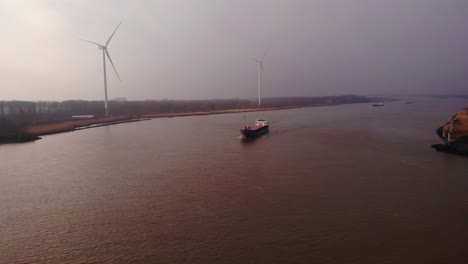 Aerial-Of-Wilson-Leith-Cargo-Ship-On-Oude-Maas-With-Wind-Turbines-In-Background-On-Cloudy-Day