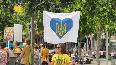 Peace-loving-pacifist,-woman-at-Brisbane-Square-holding-up-banner-with-heart-shape-coat-of-arms-of-Ukraine-during-the-demonstration-calling-for-peace-as-tension-between-Russian-and-Ukraine-rises