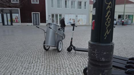 Modern-commuter-electric-scooter-parked-with-bin-trolley-in-old-Lisabon-cobble-street-Portugal