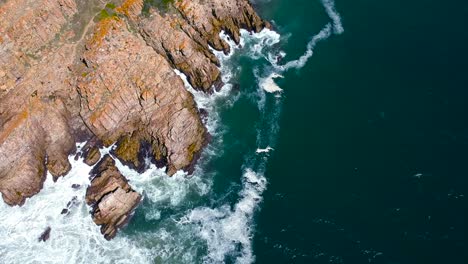 Rocky-coastline-cliff,-with-white-water-breaking-onto-shore,-scenic-vacation-destination