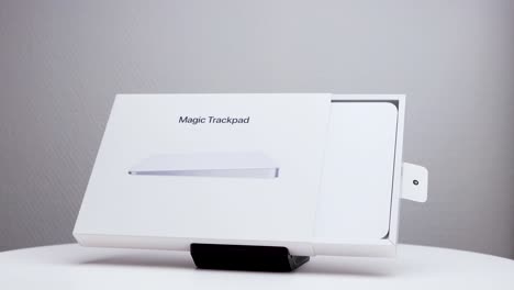 Halb-Geöffnete-Rotierende-Weiße-Verpackung-Mit-Mac-Magic-Trackpad-Auf-Ausstellungsständer-Und-Apple-Firmenlogo-An-Der-Seite