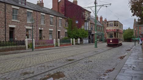 Electrified-tram-approaches-in-Victorian-town-cobbled-street,-Beamish