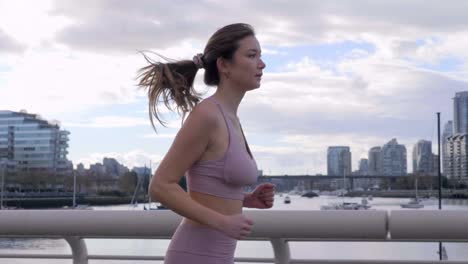 Asian-Woman-jogs-across-bridge-in-Downtown-Vancouver-BC-landscape,-Slowmo