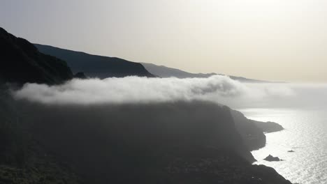 Aerial-View-of-Madeira-Island-Coastline,-Portugal,-Low-Clouds-Above-Ocean-Under-Steep-Hills-and-Misty-Horizon,-Drone-Shot