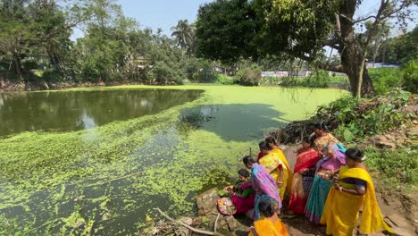 Woman-performing-rituals-near-a-green-pond-at-a-suburban-in-West-Bengal-to-celebrate-rice-ceremony-of-child-in-Bengali-style