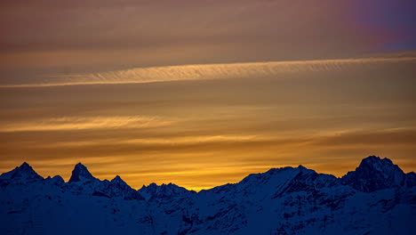 Timelapse-shot-of-cirrostratus-clouds-flying-over-snowy-mountain-range-during-epic-sunset-at-horizon