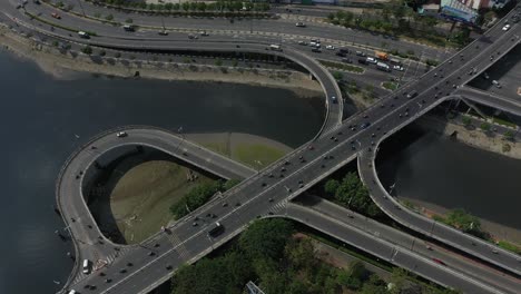 Aerial-shot-above-complex-road-system-connecting-bridges-on-and-off-ramps-and-loops-over-canal-and-river-in-Ho-Chi-Minh-City,-Vietnam-on-a-sunny-day