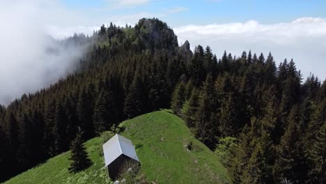 Drohnenaufnahme-Einer-Bergpassage-Mit-Einem-Kleinen-Haus,-Einem-Wald-Und-Einem-Wolkenbett