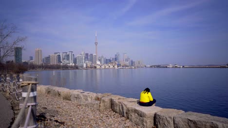 Person-in-Toronto-Trillium-Park-with-headphones-sitting-near-lake-in-bright-yellow-jacket-during-day