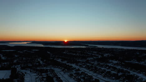 Aerial-view-over-a-snow-covered-subdivision-as-the-sun-sets-below-the-horizon