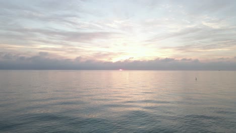 Low-flight-over-water-toward-pink-cloudy-sunrise-on-ocean-horizon
