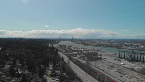 trucks-cars-traffic-travelling-along-South-perimeter-high-Delta-BC-Aerial-wide-high-above-trucking-right-moving-vehicles-below-Day-blue-sky-clouds-bridge-in-background