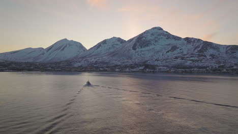 Fisherman-Boat-Sailing-To-Snowy-Fjord-Shore-In-Norway-At-Dusk,-Aerial