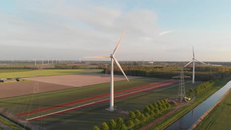 Vista-Panorámica-De-Turbinas-Eólicas-Y-Torres-Eléctricas-Con-Un-Pequeño-Río-En-Flevolanda,-Países-Bajos