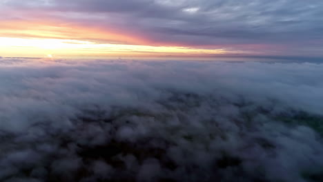 Aerial-flight-over-cloudscape-during-bright-golden-sunset-at-horizon-during-cloudy-day---view-from-airplane-window