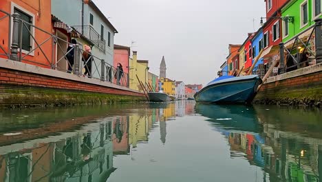 Low-angle-water-surface-pov-of-Burano-colorful-houses-and-canal-with-moored-boats,-Italy