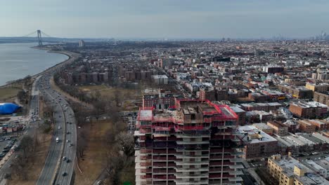 A-high-angle-view-above-a-new-high-rise-construction-site,-with-Shore-Parkway-and-the-Verrazano-bridge-in-view