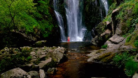 Adult-Male-Wearing-Red-Shorts-Wading-Through-Water-At-Base-Of-Fervenza-do-Toxa-Waterfalls
