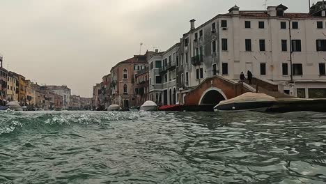 Unusual-low-angle-water-surface-pov-of-Venice-seen-from-ferry-boat-navigating-backwards,-Venice-in-Italy
