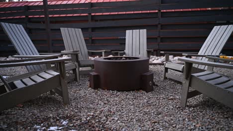Poly-lumber-patio-chairs-arranged-around-gas-fire-pit-during-the-winter,-pan