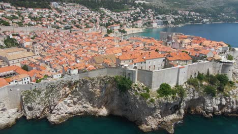 Aerial-drone-shot-over-Dubrovnik-old-town-surrounded-by-high-walls-in-Croatia-along-the-seaside-at-sunny-daytime