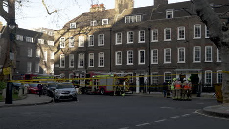 A-team-of-firemen-huddled-in-a-discussion-coordinating-their-response-to-an-emergency-at-Smiths-Square,-the-area-cordoned-off-around-the-fire-engine-to-demarcate-the-area-of-operations,-London,-UK