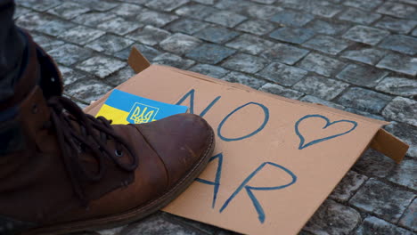 Boot-stepping-on-cardboard-sign-against-war-in-Ukraine-on-cobblestones