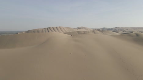Aerial-flight-toward-three-people-atop-massive-sand-dune-at-Ica,-Peru