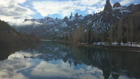 The-camera-moves-slowly-over-a-mirrored-river-surrounded-by-rocky-mountains-with-the-sun-going-down