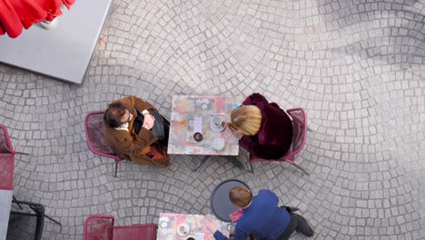 An-aerial-view-of-two-older-woman-sitting-outside-at-a-cafe-while-a-young-waitor-serves-them
