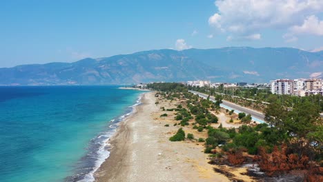 aerial-drone-panning-low-across-a-highway-towards-a-white-sandy-tropical-beach-with-the-Mediterranean-Sea-and-a-coastal-beach-town-in-Finike-Turkey-on-a-sunny-summer-day