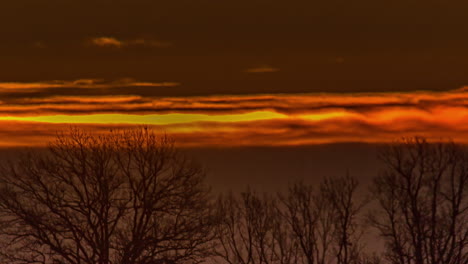 Close-up-view-of-sun-rising-over-orange-sky-through-clouds-at-dawn-in-timelapse